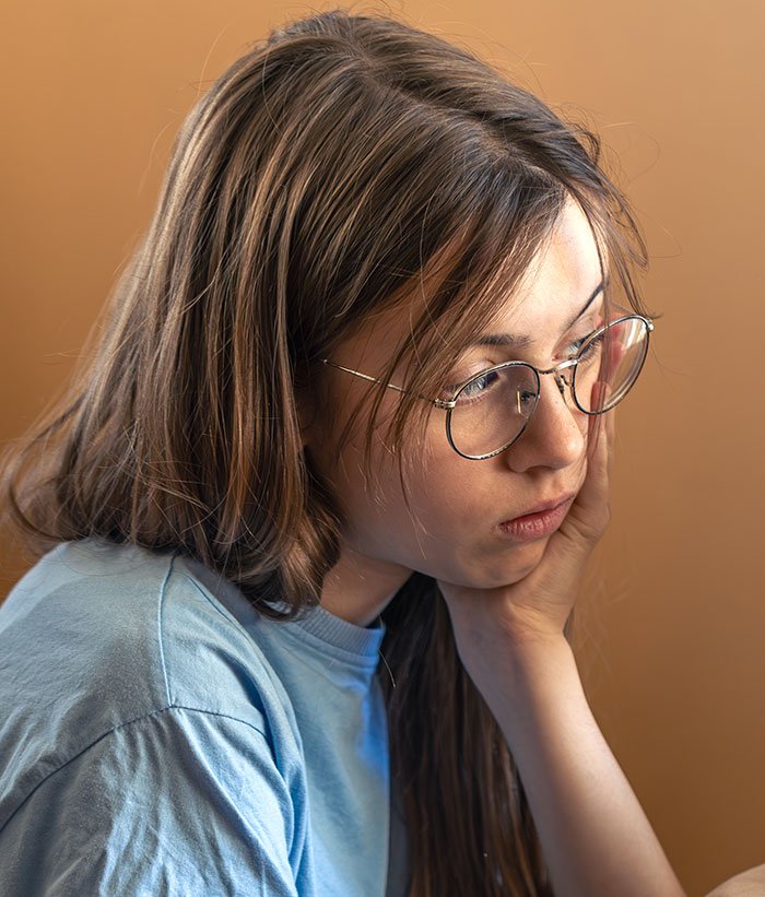 Teen girl with glasses looking thoughtful and upset, reflecting on crushed half-sister’s Christmas dreams.