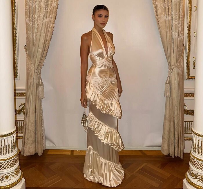 Woman in elegant satin dress standing between ornate columns and curtains, related to Melania Trump Mar-a-Lago rules controversy.