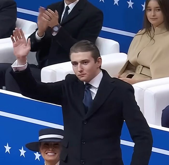 Young man in a suit waving while seated guests watch, related to Melania Trump and Mar-a-Lago rules controversy.