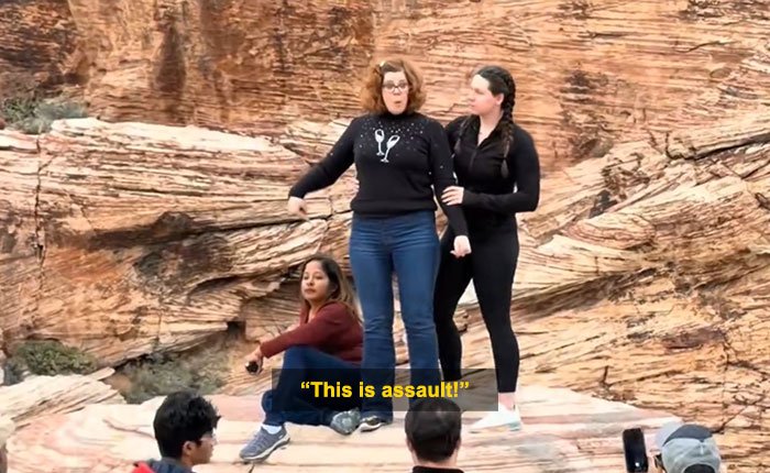 Woman blocks tourist’s shot in viral Red Rock Canyon incident with rocky desert background and bystanders nearby.