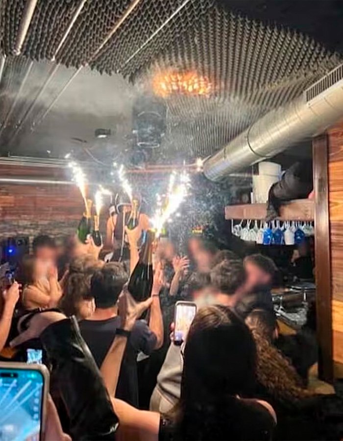Crowded Swiss ski bar with people holding champagne bottles and sparklers, possibly linked to negligence causing lethal fire.