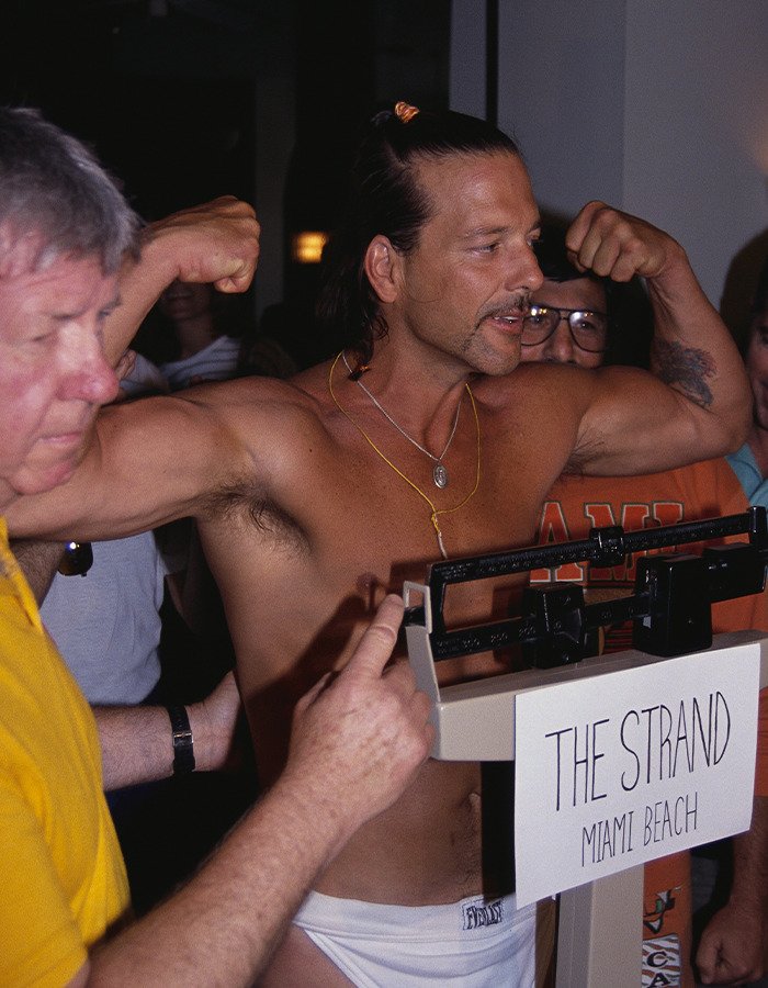 Shirtless Mickey Rourke flexing muscles while being weighed on a scale at The Strand, Miami Beach.