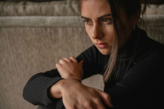 Woman sitting pensively indoors, showing emotions of betrayal and sadness related to suspicion of cheating husband and ex-girlfriend drama.