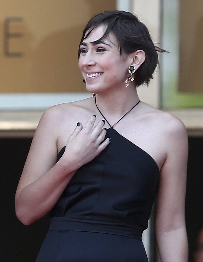 Victoria, Tommy Lee Jones’ daughter, smiling and wearing a black halter dress with statement earrings at a public event.
