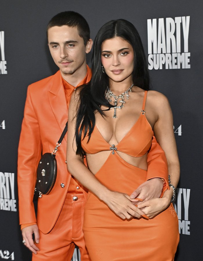Timothée Chalamet and Kylie Jenner posing together at a Marty Supreme event, both wearing orange outfits.