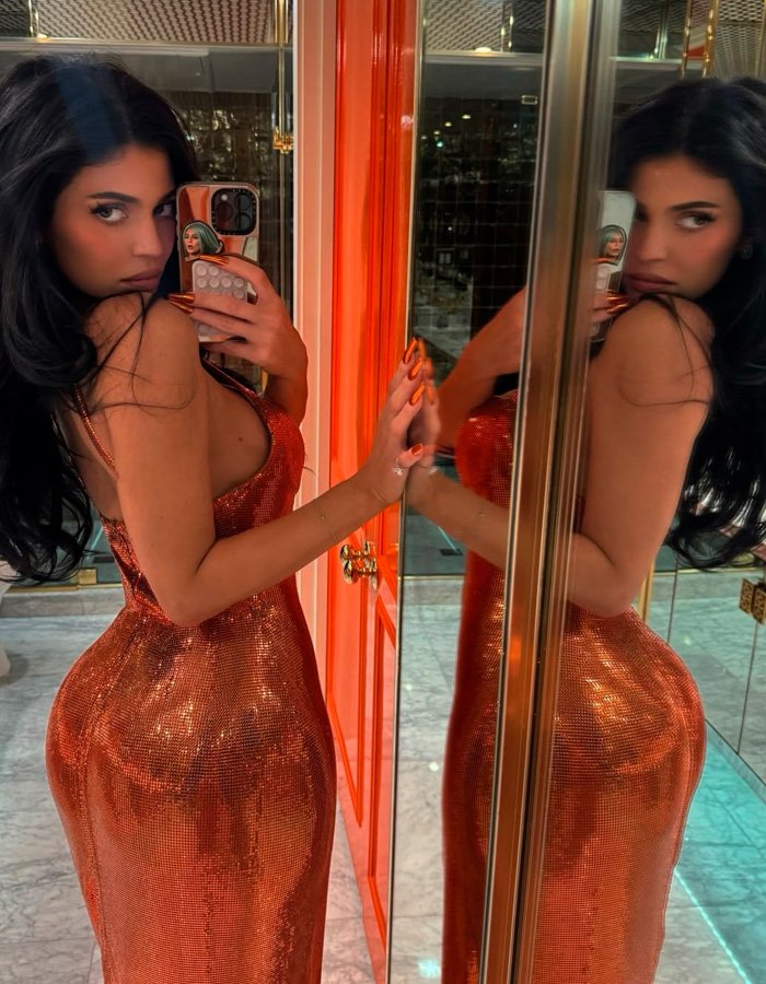 Kylie Jenner posing in a shiny orange dress taking a mirror selfie, sparking buzz with Timothée Chalamet outing.
