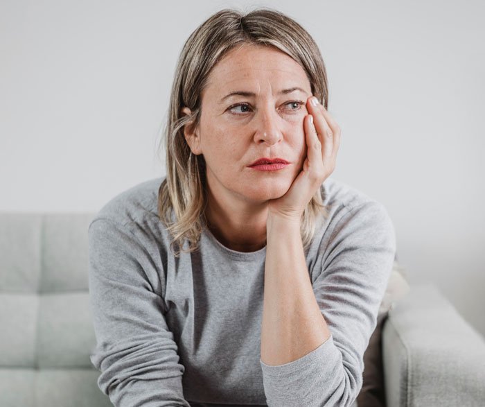 Woman sitting on a couch looking thoughtful and concerned about emptying father's estate and will issues.