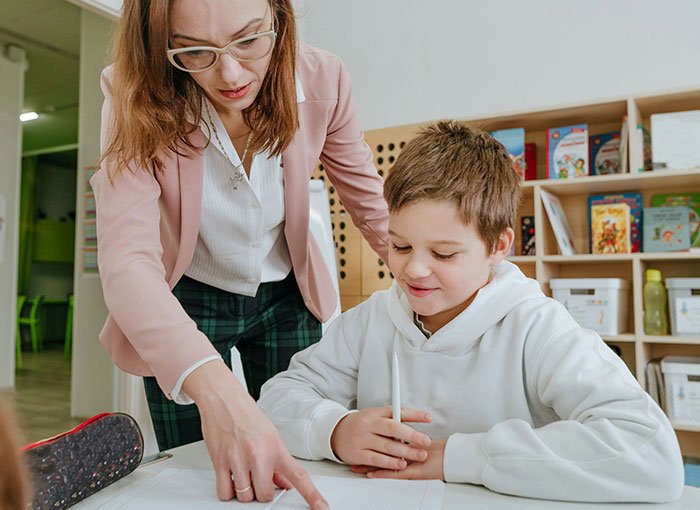 Teacher helping a smiling boy with a fun fact in a classroom, highlighting a moment of learning and discovery.