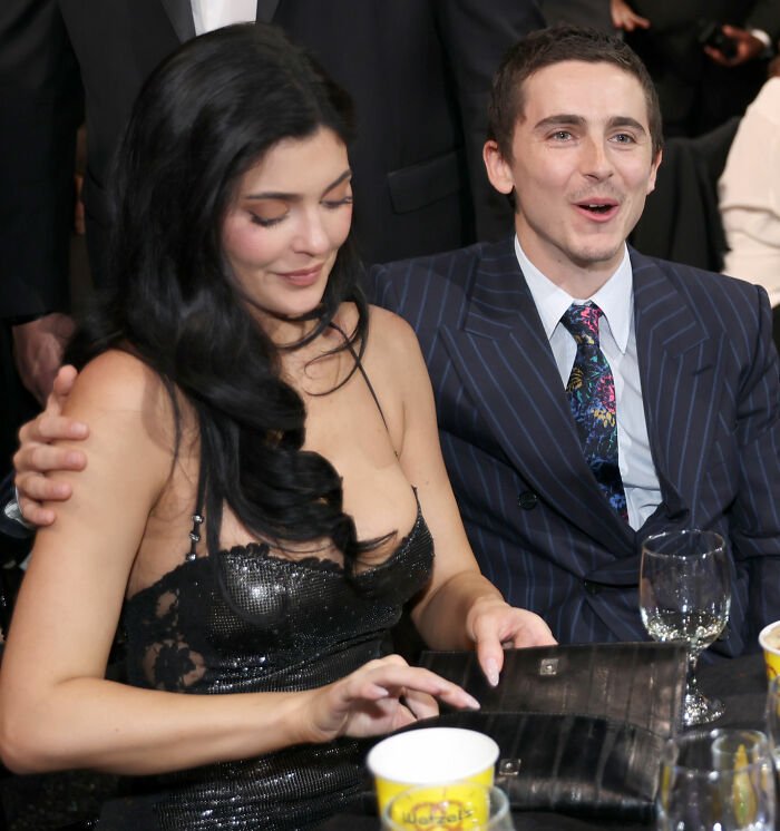 Timothée Chalamet seated beside Kylie Jenner at an event, dressed formally, engaging with the crowd around them