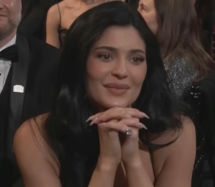 Woman with long black hair and manicured nails sitting at an event, related to video of Timothée Chalamet using Kylie's BBL.