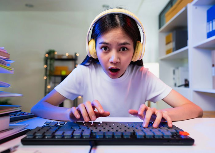 Young woman with headphones typing on keyboard, expressing surprise while discussing overused slang words to be banished in 2026.