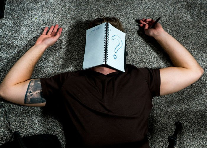 Person lying on carpet with notebook covering face showing a large question mark, representing overused slang words to banish.
