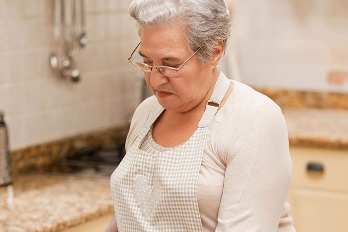 Older woman in apron making faces reacting to traditional gross food in a kitchen setting