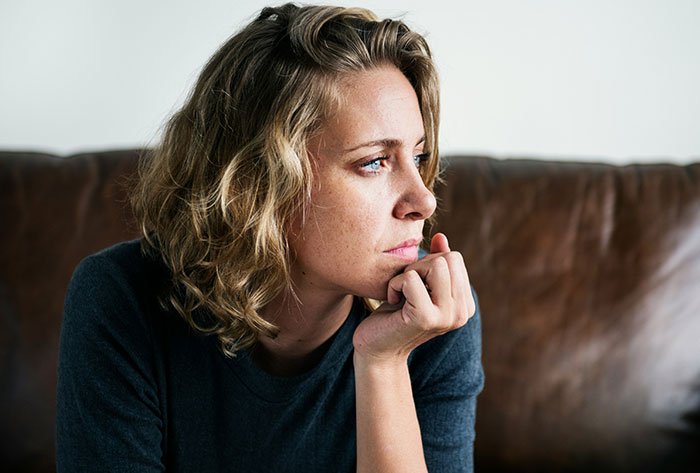 Pensive parent wonders about making daughter attend birthday, woman gazing thoughtfully on a couch