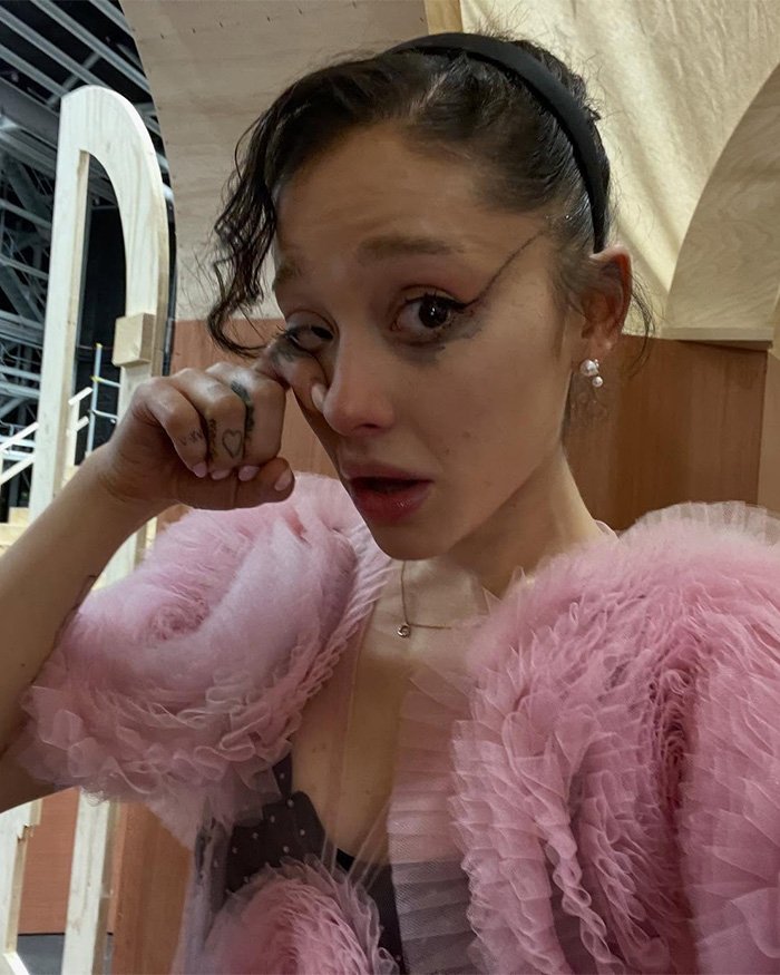 Backstage close-up of a tearful woman in pink ruffled costume with smeared eye makeup on Wicked set