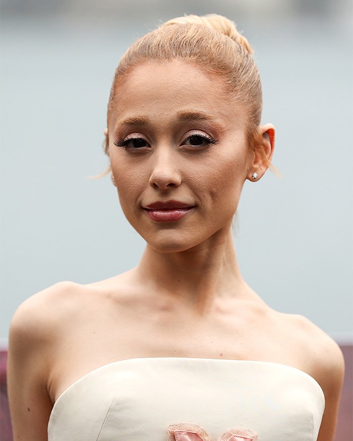 Close-up of a young woman in a strapless white dress with hair in a bun on Wicked set, subtle makeup, neutral background
