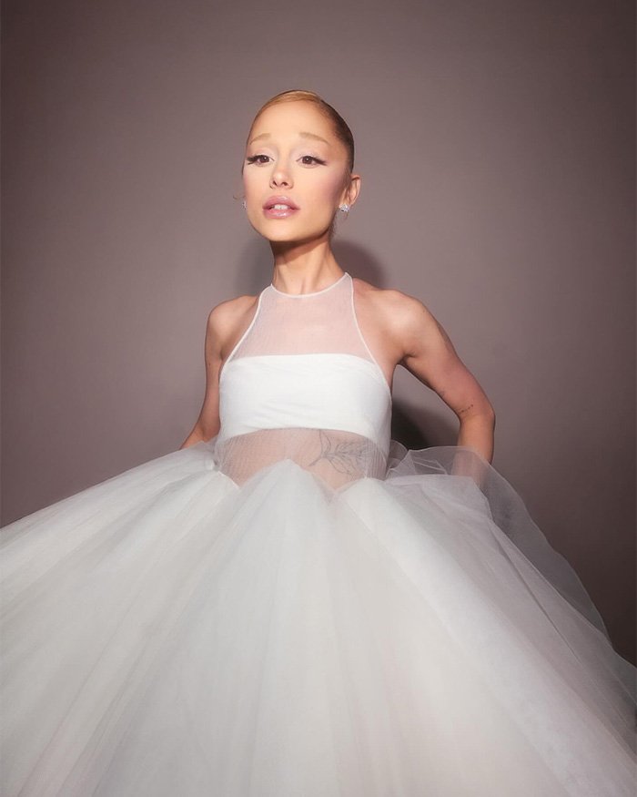 Wicked set photo of an actor in a white tulle gown with high bun, soft makeup, posed against a neutral backdrop