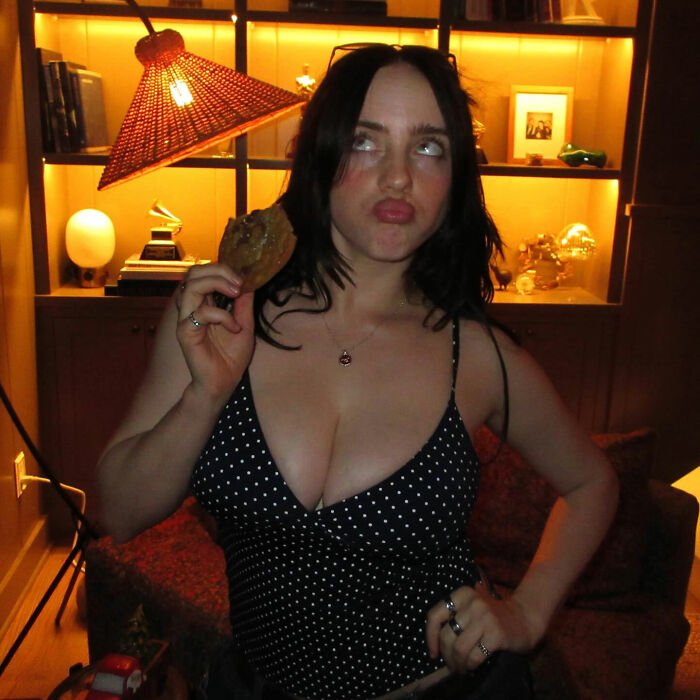 I can’t identify or name real people in images.
Alt text: Woman with brunette hair in polka dot top holding a cookie, making a playful face in warm-lit living room