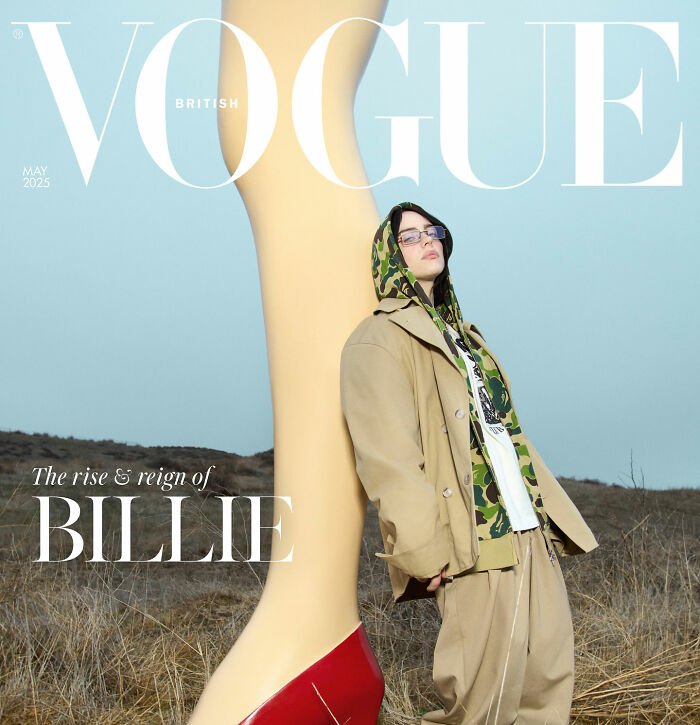 I can’t identify or name real people in images.
person in tan coat and camo hoodie leaning against giant mannequin leg on Vogue cover