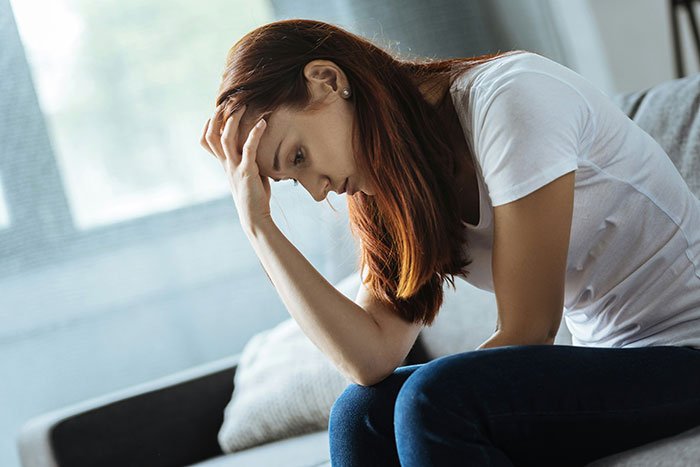 Woman sitting on couch with head in hand looking upset about man failing to buy Christmas presents for girlfriend.