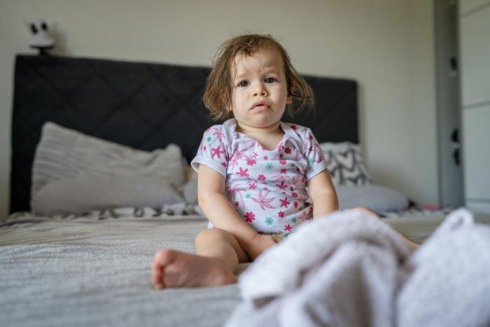 Toddler looking uncomfortable on bed, highlighting woman horrified MIL didn't change the kid's diaper all day.