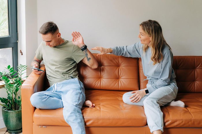 Woman upset and refusing communication with man on couch, illustrating conflict over MIL not changing kid's diaper all day.