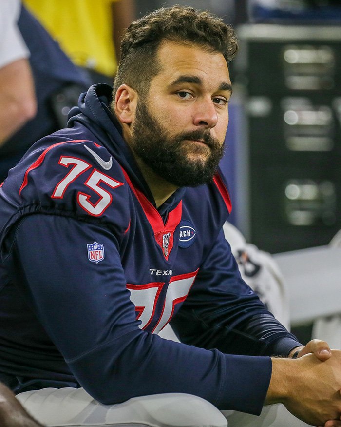 Former NFL star sitting on the bench during a game, wearing a dark blue jersey with number 75 visible.