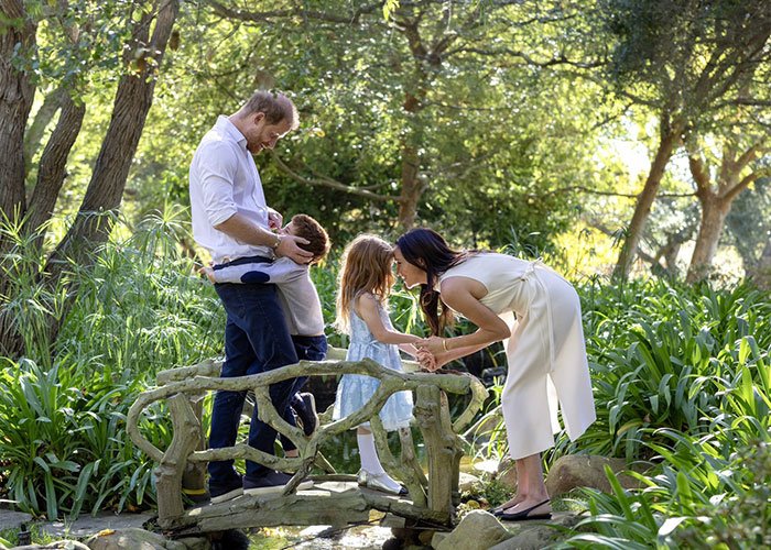 Family moment on a small bridge in a lush garden, highlighting Meghan Markle’s alleged rift with mom Doria theories.