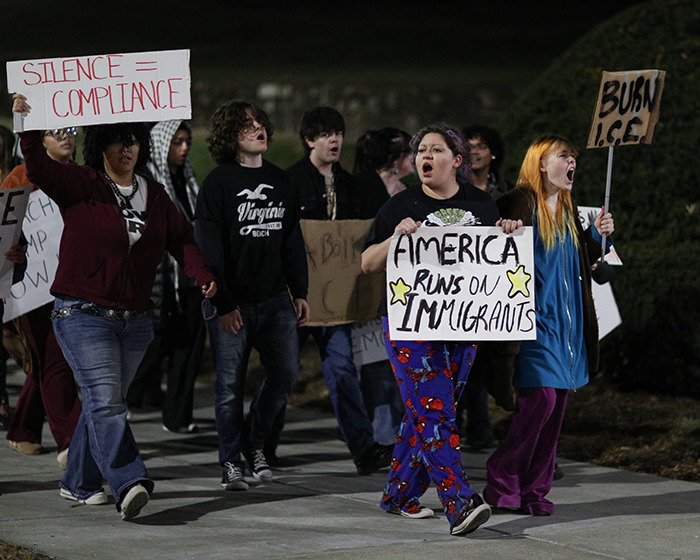 Protesters march at night holding signs about immigrants and ICE during a demonstration over the ICE slaying incident.