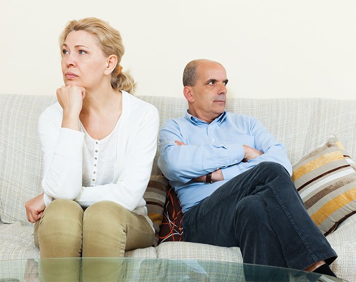 A middle-aged couple sitting on a couch, looking upset and avoiding eye contact, reflecting distrust in-laws and grandchild safety.