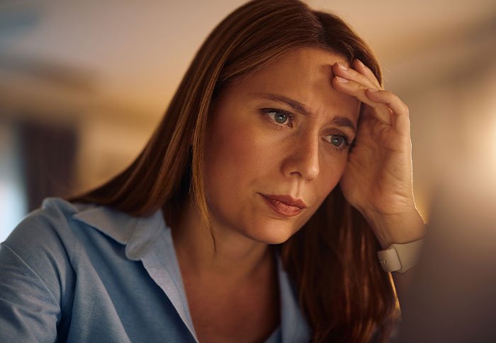 Worried mother sitting at a desk, contemplating the school request to make her twins less similar for easier distinction.