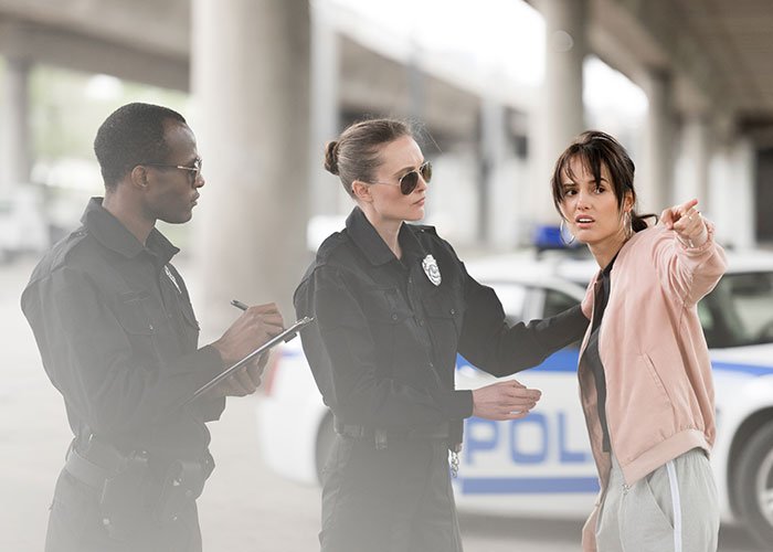 Two police officers questioning a distressed woman about a fiancée’s obsession with her bully stalking issue outdoors.