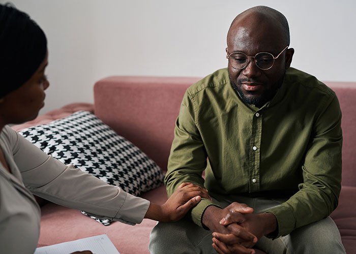 Man in glasses and green shirt looking down while woman comforts him, illustrating fiancée’s obsession with her bully affecting relationships.