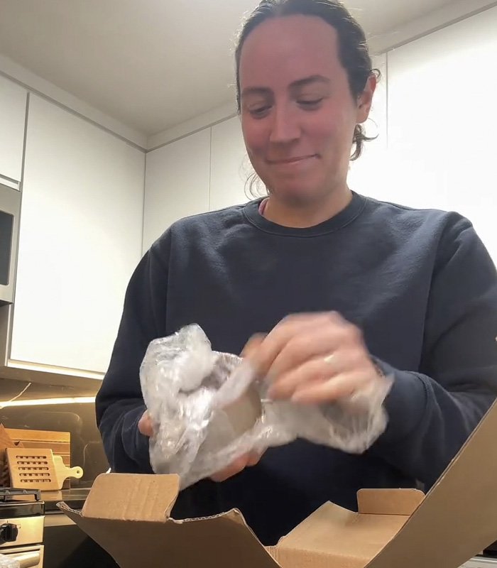 Person unwrapping a mug gift from fiancé, sparking a huge relationship debate online in a modern kitchen setting.