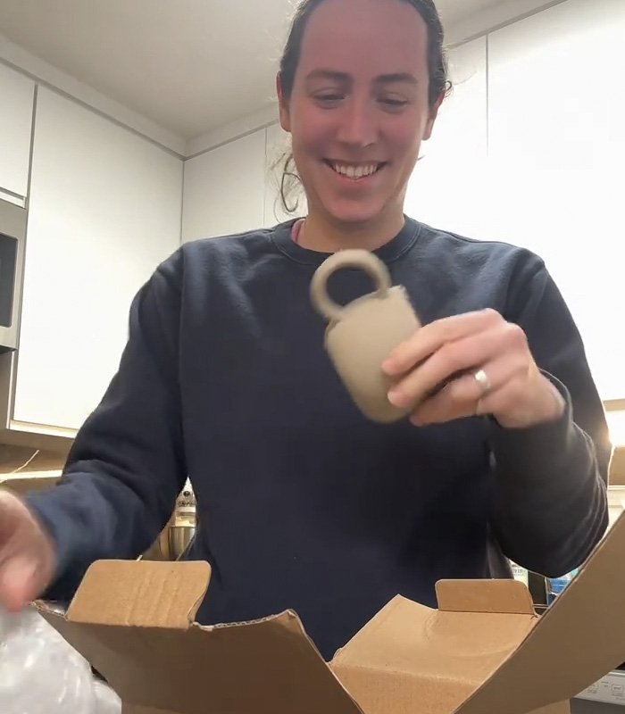 Woman smiling while holding a mug gift from fiancé, sparking a huge relationship debate online.