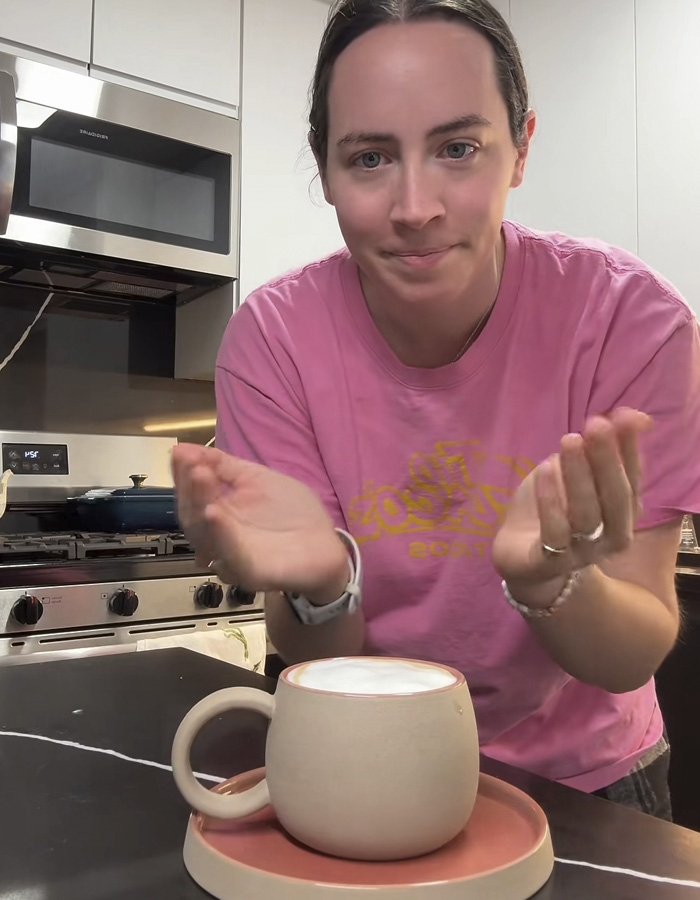 Woman in pink shirt presenting a ceramic mug gift sparking a huge relationship debate online about fiancé’s intentions.