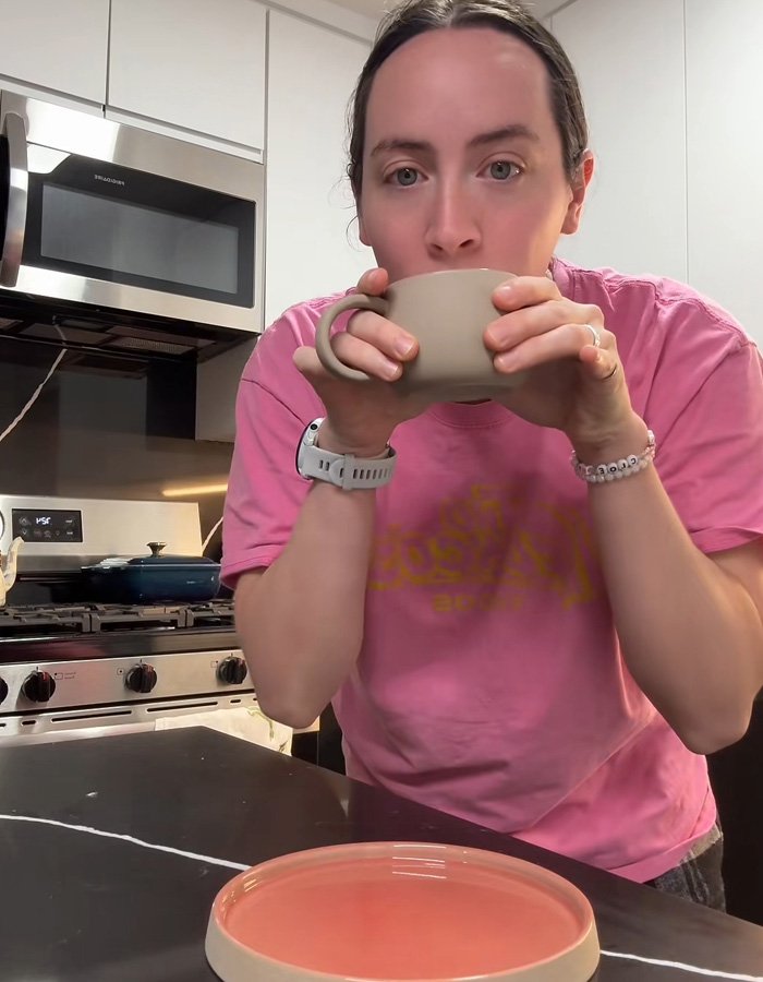 Person in a pink shirt drinking from a mug gift sparking a huge relationship debate online in a modern kitchen setting
