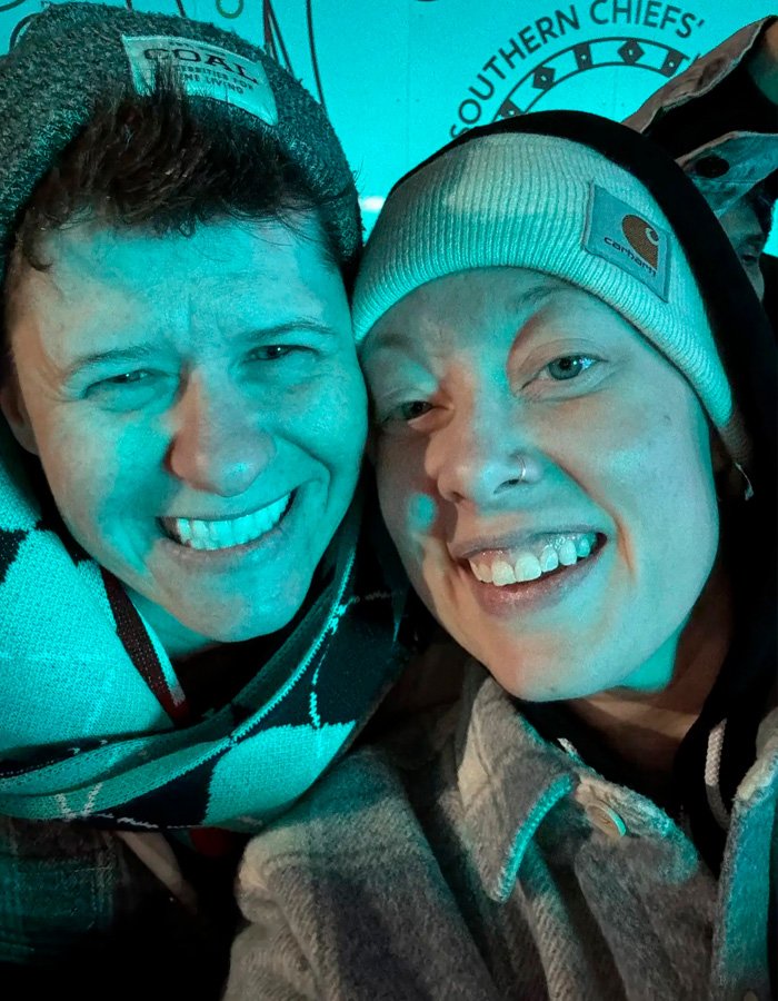 Two people smiling closely together wearing winter hats and jackets, related to Renee Good’s wife and fatal ICE incident.