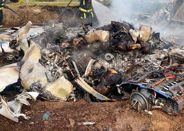 Wreckage of a plane crash site with firefighters extinguishing smoke, related to famous singer's tragic accident.