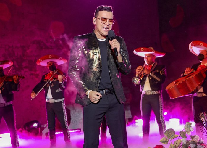 Famous singer performing on stage with mariachi band, under dramatic purple lighting and smoke effects.