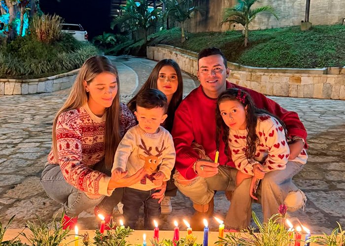 Family gathered outdoors at night, wearing festive sweaters, lighting candles in a heartfelt moment for famous singer.