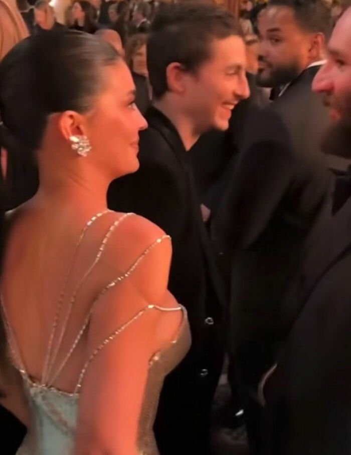Kylie Jenner and Timothée Chalamet at Golden Globes event with other stars in a dimly lit social setting.