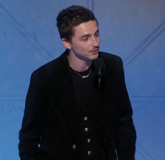 Timothée Chalamet speaking at a microphone during an event, linked to lip reader revealing Golden Globes fight.