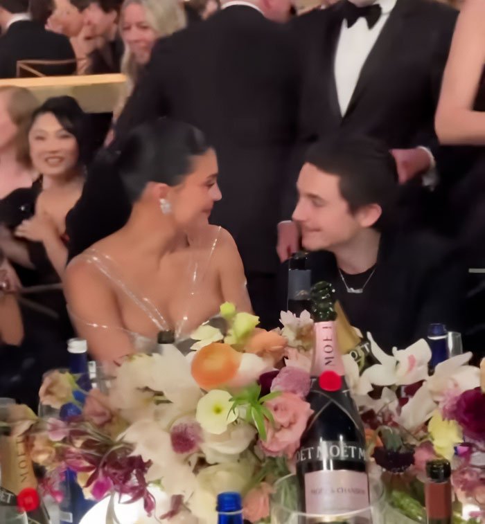 Timothée Chalamet and Kylie Jenner at the Golden Globes seated together amidst floral centerpiece and champagne bottles