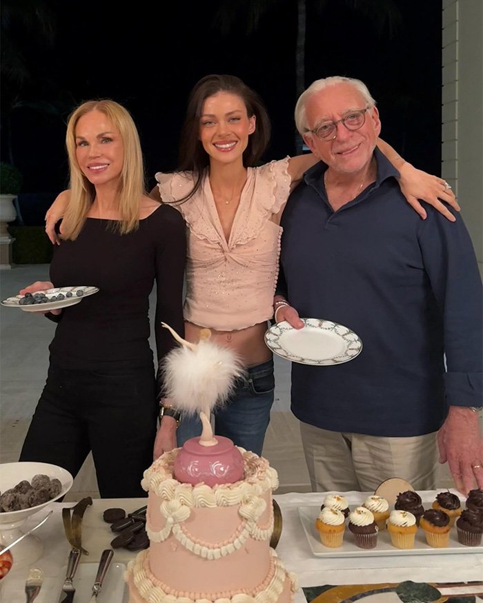 Three people smiling at a gathering with dessert plates and a cake, related to Brooklyn Beckham family drama update.