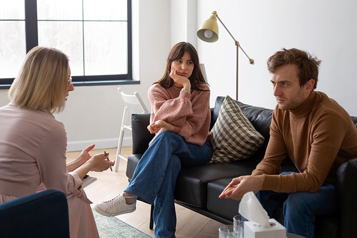 Couple discussing open marriage agreement with a counselor in a modern room, expressing concern and contemplation.
