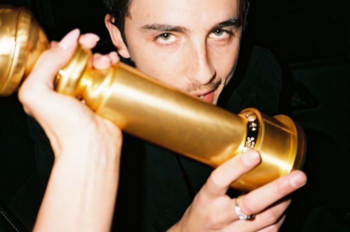 Timothée Chalamet holding a Golden Globe award close to his face in a dimly lit setting after fight news.