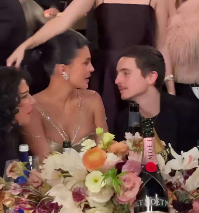 Timothée Chalamet and Kylie Jenner seated at a floral-decorated table during a formal event with drinks nearby.