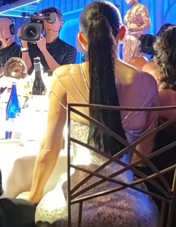 Kylie Jenner sitting in an unusual Golden Globes seat wearing a sparkling dress with a long ponytail at a formal event.