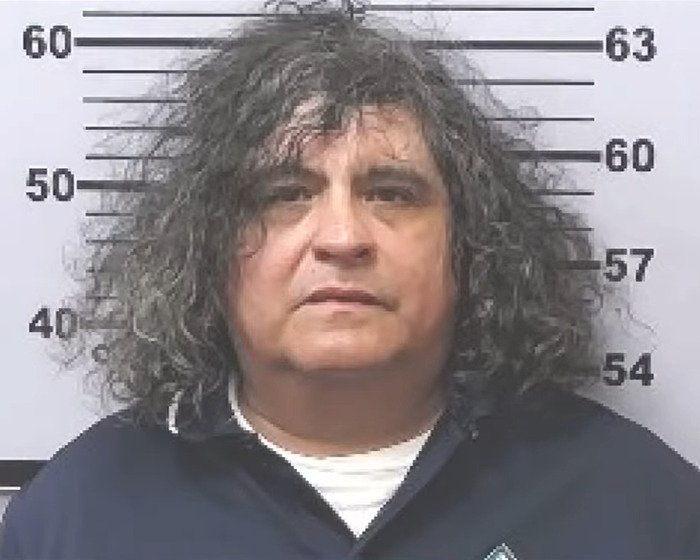 Mugshot of a man with curly hair against a height chart related to girl abandoned in mobile home case.